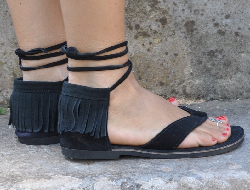 May include: Black leather sandals with fringe detailing and ankle ties. The sandals have a flat sole and are made of a soft, supple leather.