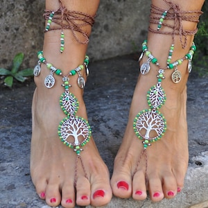 Puede incluir: Joyería de pie con cuentas verdes y plateadas con un diseño de árbol de la vida. La joyería está atada alrededor del tobillo y tiene una larga hebra de cuentas que cuelga hasta los dedos de los pies.