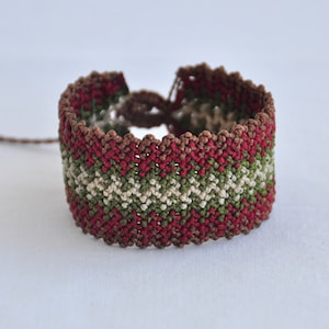 May include: A red, green and brown friendship bracelet with a chevron pattern.