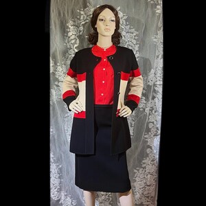 May include: A black and beige cardigan with red trim and a black skirt. The cardigan has a button closure and a collar. The skirt is knee-length and has a straight silhouette.