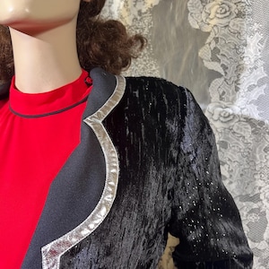 May include: A black velvet blazer with a silver trim. The blazer has a textured surface and a slightly curved collar.