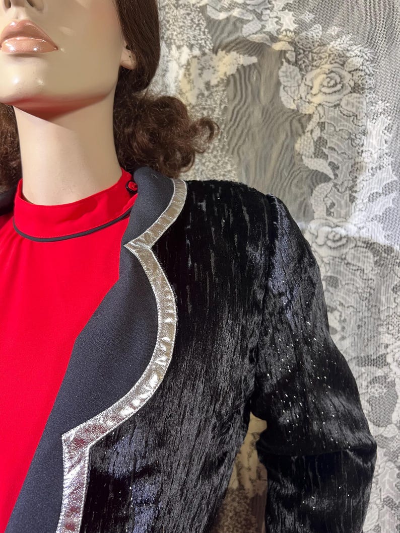 May include: A black velvet blazer with a silver trim. The blazer has a textured surface and a slightly curved collar.