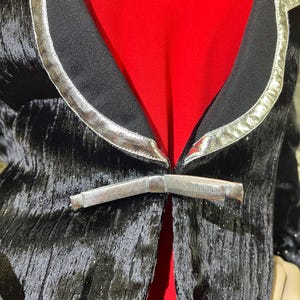 May include: A black velvet blazer with silver trim and a silver buckle closure. The blazer has a textured, sparkly finish.