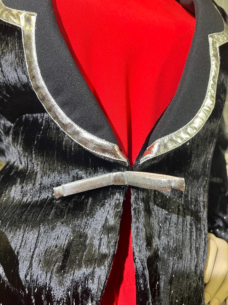 May include: A black velvet blazer with silver trim and a silver buckle closure. The blazer has a textured, sparkly finish.