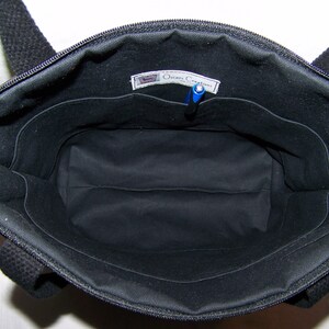 May include: Open view of a black tote bag with a zipper closure and black handles. The interior is black with multiple pockets and a pen. The bag has a label that reads "Oceans Creations".