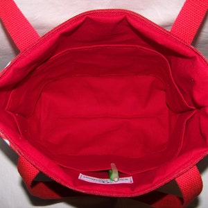 Pu&ograve; includere: Vista interna di una borsa tote rossa con chiusura a zip e manici rossi. L'interno &egrave; rosso vivo con pi&ugrave; tasche. Il tessuto esterno presenta un motivo floreale bianco. Si vede una penna verde.