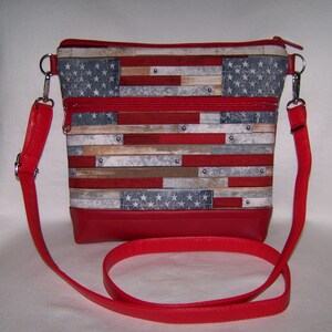 Pu&ograve; includere: Borsa a tracolla rettangolare con base e cinturino in pelle rossa. Il corpo principale della borsa presenta una stampa che ricorda la bandiera americana, con strisce rosse e bianche e un campo blu di stelle. Cerniere e hardware argentati completano il design.