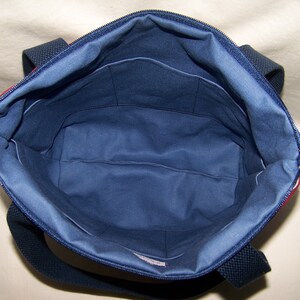 Pu&ograve; includere: Vista aperta di una borsa tote blu navy con chiusura a zip. L'interno &egrave; blu navy con pi&ugrave; tasche. La borsa ha manici blu navy e un accento a righe rosse e bianche lungo il bordo superiore.