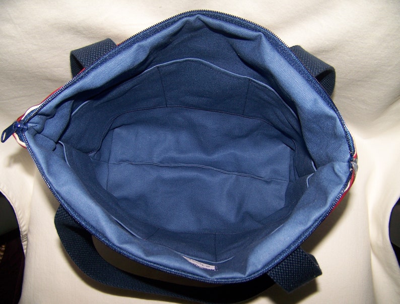 Pu&ograve; includere: Vista aperta di una borsa tote blu navy con chiusura a zip. L'interno &egrave; blu navy con pi&ugrave; tasche. La borsa ha manici blu navy e un accento a righe rosse e bianche lungo il bordo superiore.