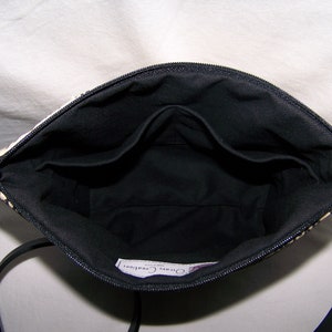 Pu&ograve; includere: Vista interna di una borsa a fantasia bianca e nera con interno nero. La borsa ha una chiusura a zip e un cinturino nero. L'interno presenta pi&ugrave; tasche. La borsa &egrave; progettata per trasportare l'essenziale.