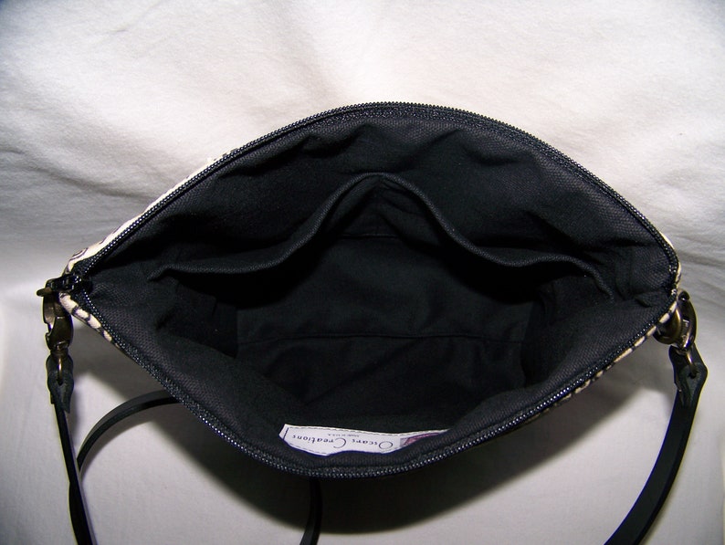 Pu&ograve; includere: Vista interna di una borsa a fantasia bianca e nera con interno nero. La borsa ha una chiusura a zip e un cinturino nero. L'interno presenta pi&ugrave; tasche. La borsa &egrave; progettata per trasportare l'essenziale.