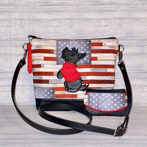 Pu&ograve; includere: Una borsa a tracolla e un portafoglio abbinato con un design ispirato alla bandiera americana. La borsa ha un cinturino e una base in pelle nera, con un cane ricamato con una camicia rossa. Il portafoglio ha un bordo rosso.