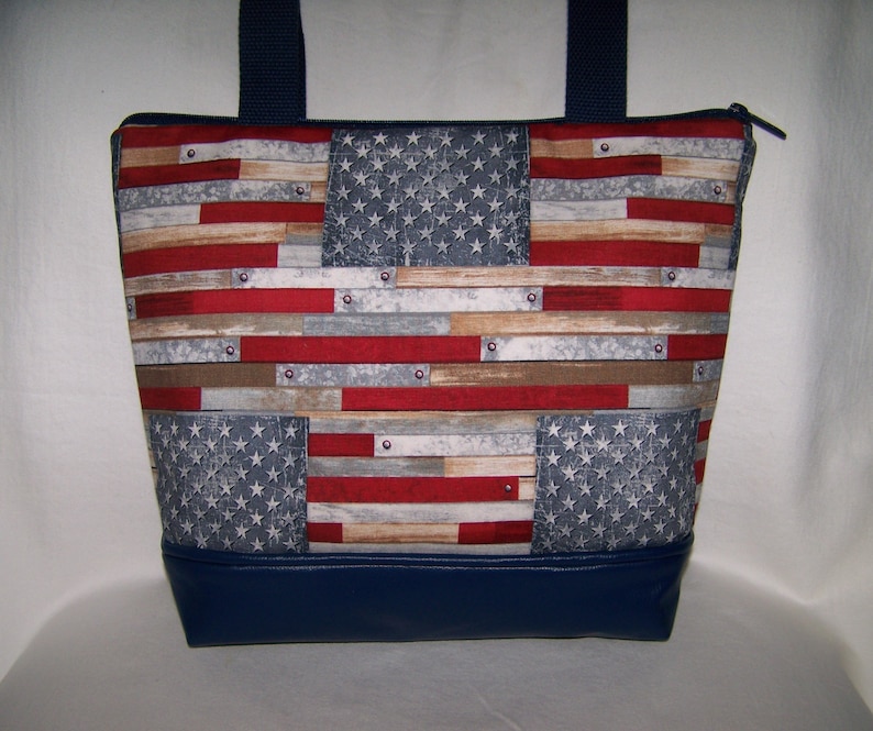 Pu&ograve; includere: Una borsa tote con un design patriottico. La borsa presenta un motivo che ricorda la bandiera americana, con strisce rosse e bianche e un campo blu di stelle. Il fondo della borsa &egrave; blu navy tinta unita e ha manici blu navy.