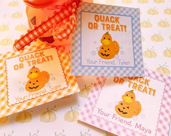 May include: An orange rubber ducky with a pumpkin-carved face, adorned with a decorative ribbon, and accompanied by three gift tags. The tags read "QUACK OR TREAT!" and feature a duck-pumpkin graphic, with personalized names.