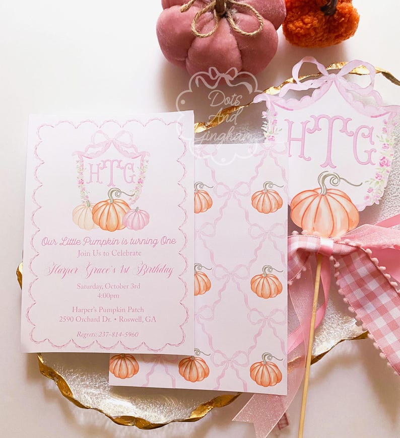 May include: Pink and white invitation suite with pumpkin illustrations. The invitation reads "Our Little Pumpkin is turning One" and includes event details. A decorative pumpkin-themed cake topper and decorative pumpkins are also present.