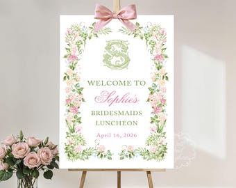 May include: A welcome sign for a bridesmaids luncheon, featuring floral accents and a pink bow. The sign reads "Welcome to Sophie's Bridesmaids Luncheon April 16, 2026". The sign is displayed on a wooden easel.