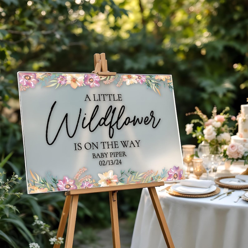 May include: A light blue baby shower sign with floral accents and the text "A Little Wildflower is on the way Baby Piper 02/13/24".