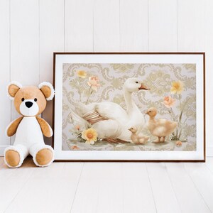 May include: A framed print featuring a white goose with three goslings amidst yellow and peach flowers. The artwork has a vintage aesthetic, with a patterned background and soft color palette. The print is displayed next to a teddy bear.