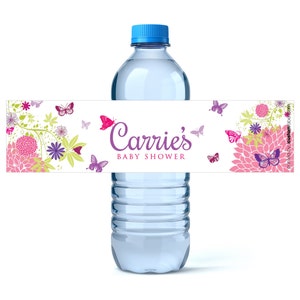 May include: A clear water bottle with a blue cap and a decorative label. The label features the text "Carrie's BABY SHOWER" in purple script, surrounded by pink and purple butterflies and floral designs.