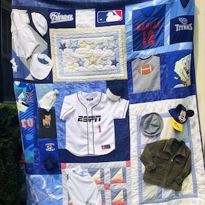 May include: A blue and white patchwork quilt with various sports team logos and baby items. The quilt features logos for the Patriots, Kansas City Chiefs, and Tennessee Titans. There are also baby clothes, a baseball cap, and a stuffed animal.