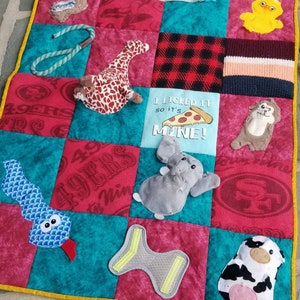 Pu&ograve; includere: Un tappetino da gioco trapuntato multicolore per cani con diverse trame e forme. Il tappetino presenta un tessuto rosso, bianco e blu con il testo "I licked it so it's mine!" e una grafica a fetta di pizza. Altre caratteristiche includono un serpente, una giraffa, un elefante, una mucca, un'anatra e un giocattolo a forma di osso.