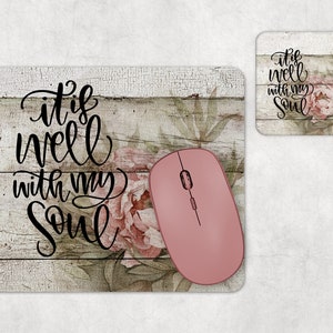 May include: A mouse pad with a wood grain background and pink flowers. The text "it is well with my soul" is written in black cursive lettering. A pink computer mouse is on the pad.