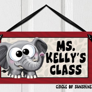 May include: A red wooden sign with a cartoon elephant with big eyes and a white background with gray leaves. The sign says "MS. KELLY'S CLASS" and "CIRCLE OF SUNSHINE™".