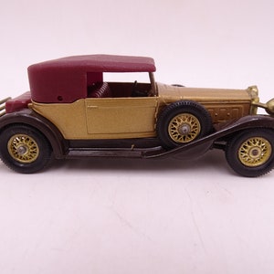 May include: A gold and brown toy car with a red convertible top. The car has a detailed grill and headlights.