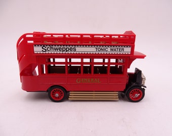 Puede incluir: Un juguete de autobús de dos pisos rojo con un letrero blanco "Schweppes Tonic Water" en la parte superior y un letrero dorado "General" en el lateral.