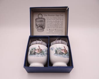 May include: A set of two white porcelain Royal Worcester egg coddlers with metal screw-on lids, featuring a bird and floral illustration. The items are housed in a blue cardboard box with an instructional insert titled The Premier Egg Cup.