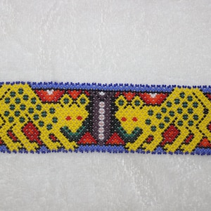 Puede incluir: Un brazalete de cuentas con un borde azul y dos figuras de animales amarillas y verdes con manchas negras. Las figuras se miran y tienen detalles rojos y blancos.