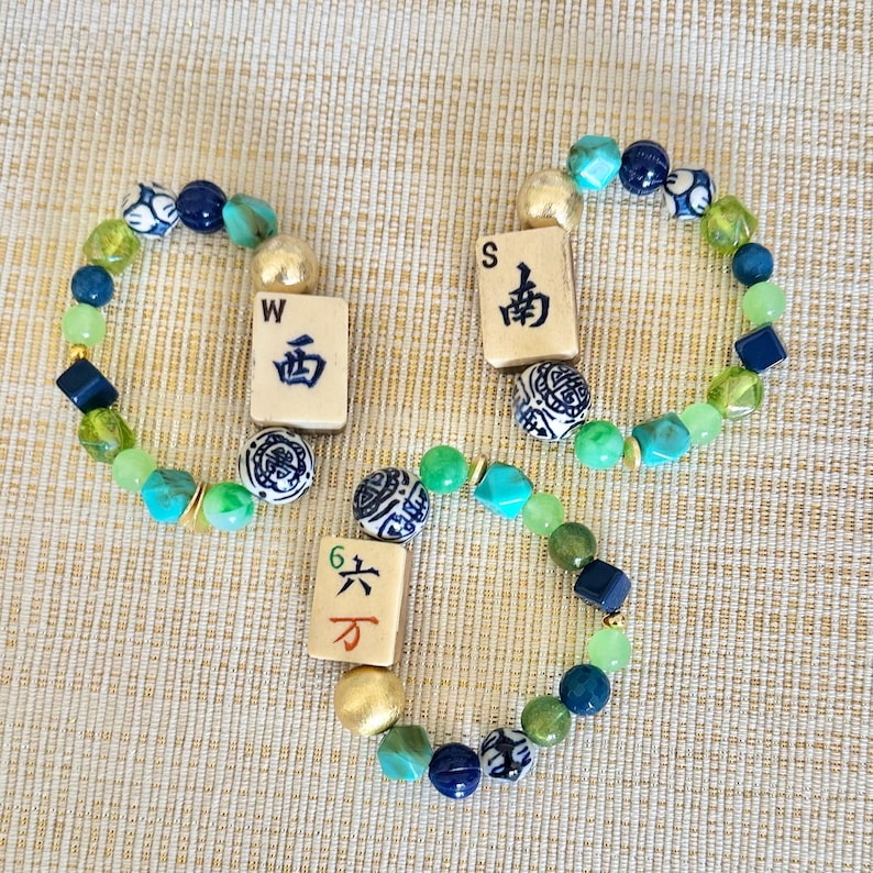 Puede incluir: Tres pulseras de cuentas con cuentas verdes, azules y doradas. Cada pulsera incluye una ficha de Mahjong diferente con caracteres chinos y las letras "W" y "S".