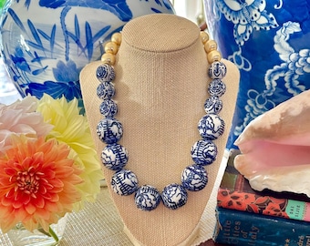 May include: A necklace featuring large, round blue and white porcelain beads with intricate patterns. The necklace is displayed on a mannequin bust. The design is interspersed with smaller, light-coloured beads. The necklace is a statement piece.