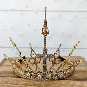 May include: A gold crown with a silver cross in the center, adorned with clear and amber rhinestones and pearl-like beads.