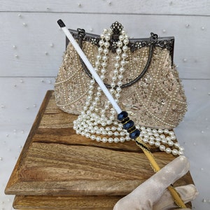 May include: A beaded clutch purse with a gold clasp and a pearl and black beaded cigarette holder.