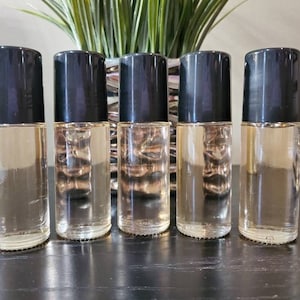 May include: Five clear glass roller bottles with black caps. The bottles are filled with a light-colored liquid.