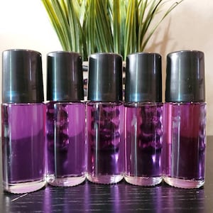 May include: Six small glass bottles with black roll-on tops filled with a purple liquid. The bottles are lined up in a row on a dark surface.