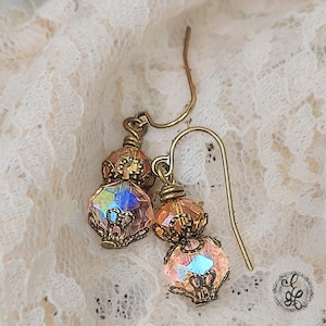 May include: A pair of vintage-style earrings with iridescent crystal beads and ornate bronze-colored metalwork. The earrings feature a combination of round and faceted beads, suspended from curved ear wires. The design evokes a sense of antique charm and elegance.