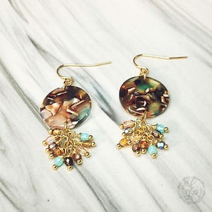 May include: Gold dangle earrings with a brown and green marbled round disc and a fringe of gold and turquoise beads.