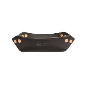 May include: A black leather catch-all tray with copper rivets. The tray has a rectangular shape with angled sides and the text "HARDMILL" is embossed on the front. This tray is suitable for storing small items.