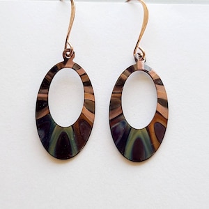 May include: A pair of oval-shaped earrings with a swirling pattern in shades of brown, green, and black. The earrings have a rose gold hook.