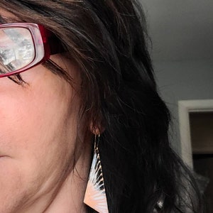 May include: A pair of dangle earrings with a geometric, triangular design. The earrings are made of metal and have a white, black, and peach color scheme.