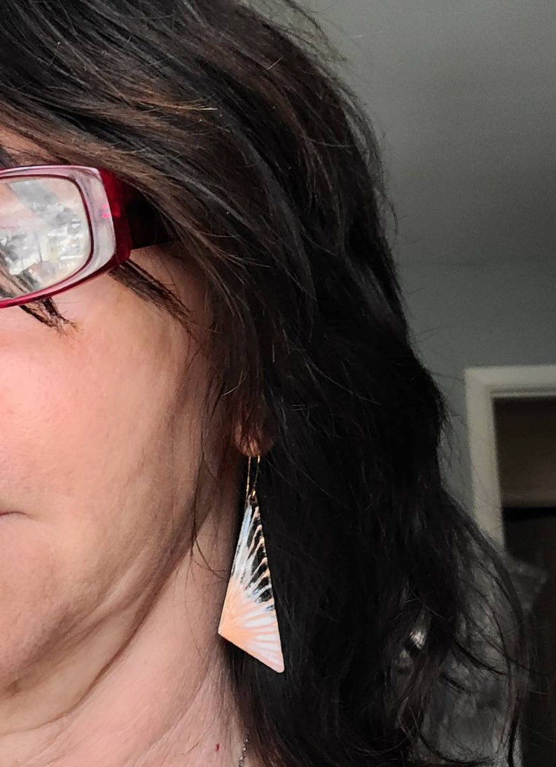 May include: A pair of dangle earrings with a geometric, triangular design. The earrings are made of metal and have a white, black, and peach color scheme.