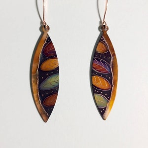May include: A pair of copper earrings with a black background and colorful leaf designs. The leaves are in shades of orange, yellow, green, and purple.