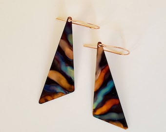May include: A pair of abstract geometric earrings. Each earring is a copper-colored triangle with a colorful, wavy pattern in shades of blue, orange, and brown. The earrings have copper-colored ear wires.