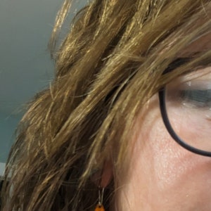 May include: A pair of dangle earrings with a teardrop-shaped pendant. The pendant is made of ceramic and features a blue, orange, and yellow design.