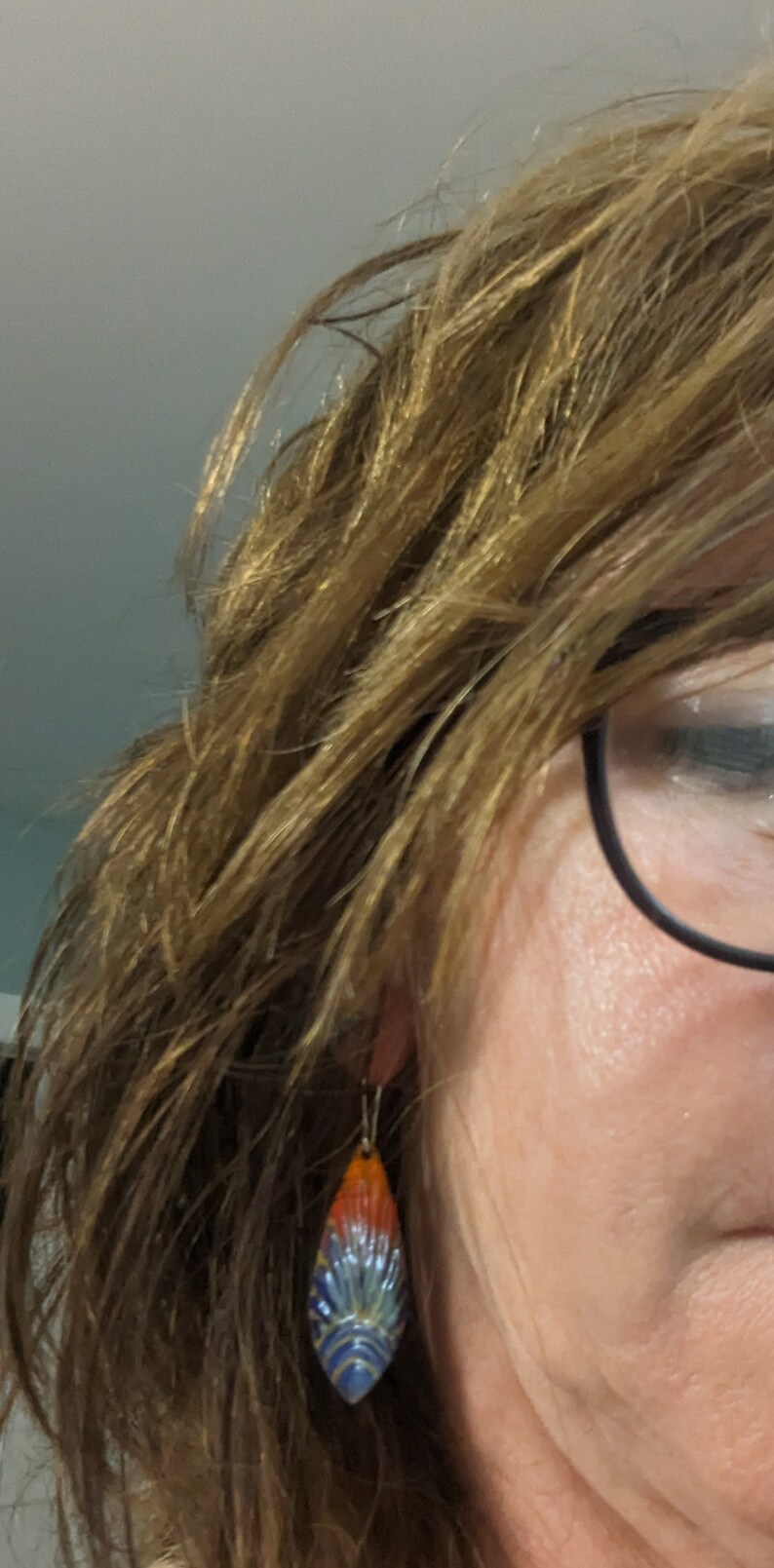 May include: A pair of dangle earrings with a teardrop-shaped pendant. The pendant is made of ceramic and features a blue, orange, and yellow design.