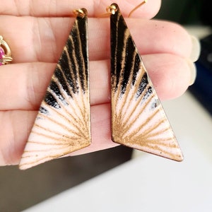 May include: A pair of gold, black, and white geometric earrings with a sunburst design.