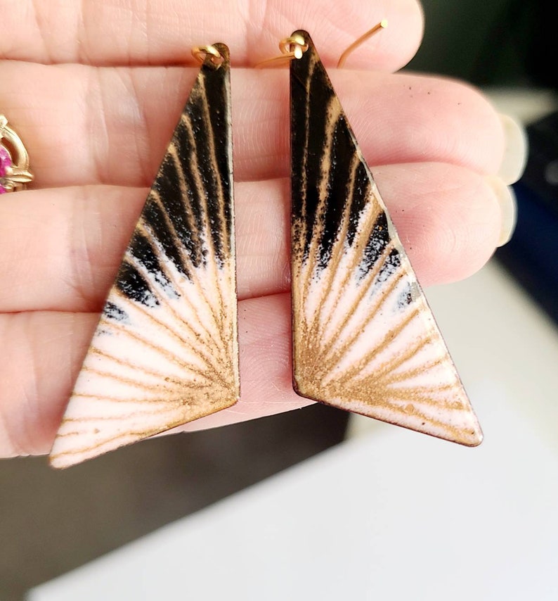 May include: A pair of gold, black, and white geometric earrings with a sunburst design.