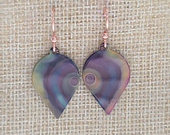 May include: A pair of dangle earrings with a teardrop-shaped design. The earrings are made of a dark purple, blue, and green material with a swirling pattern. The earrings have a copper-colored hook.